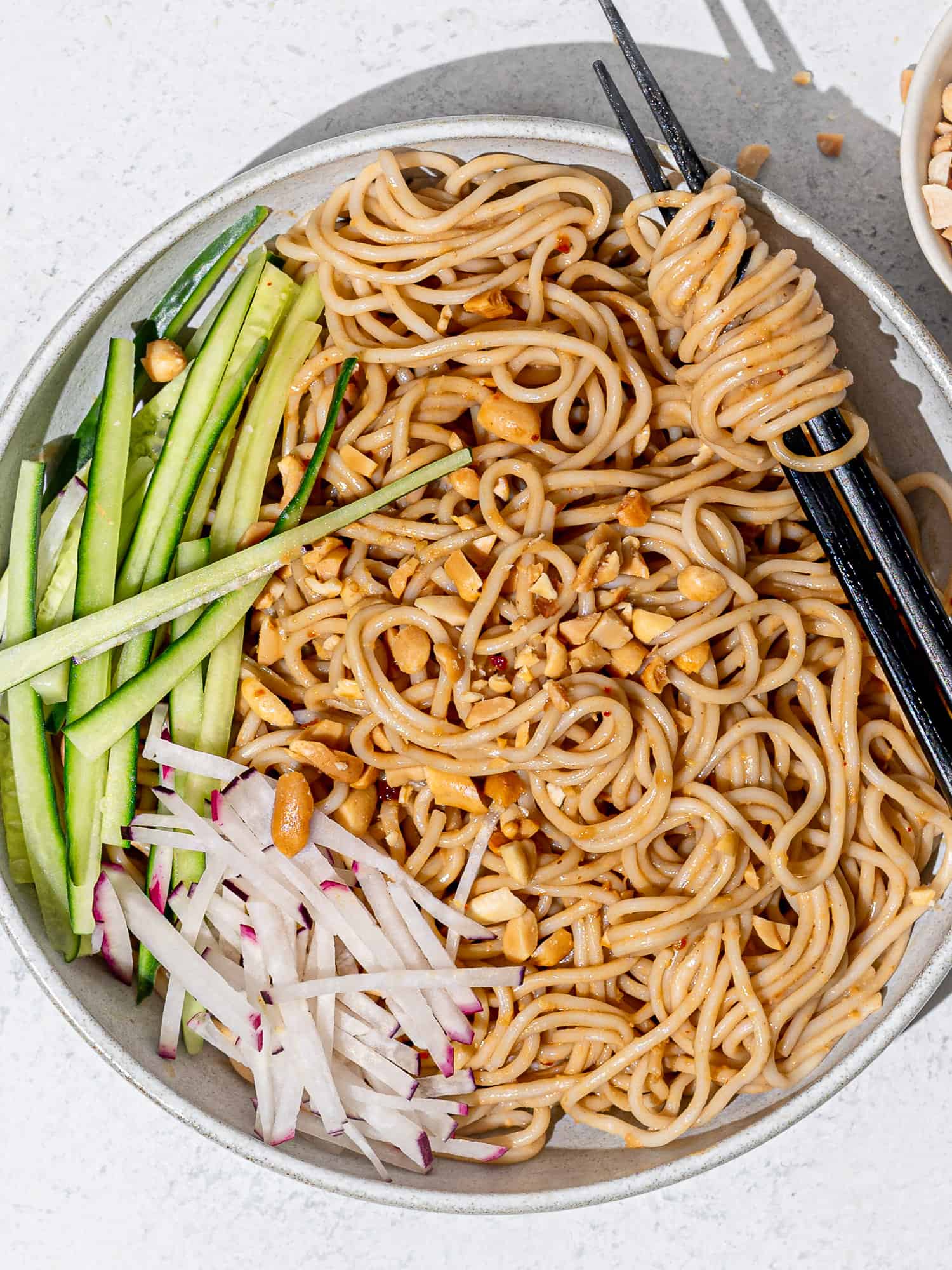 Takeout-style sesame noodles served in bowl with cucumbers and radishes