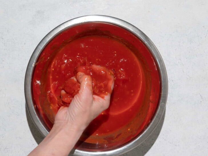 Crushing tomatoes in bowl by hand 