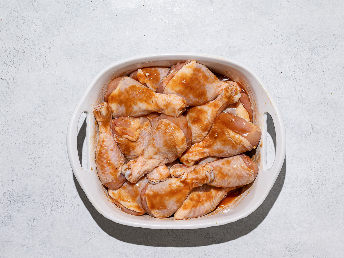 Chicken drumsticks marinating in white baking dish. 