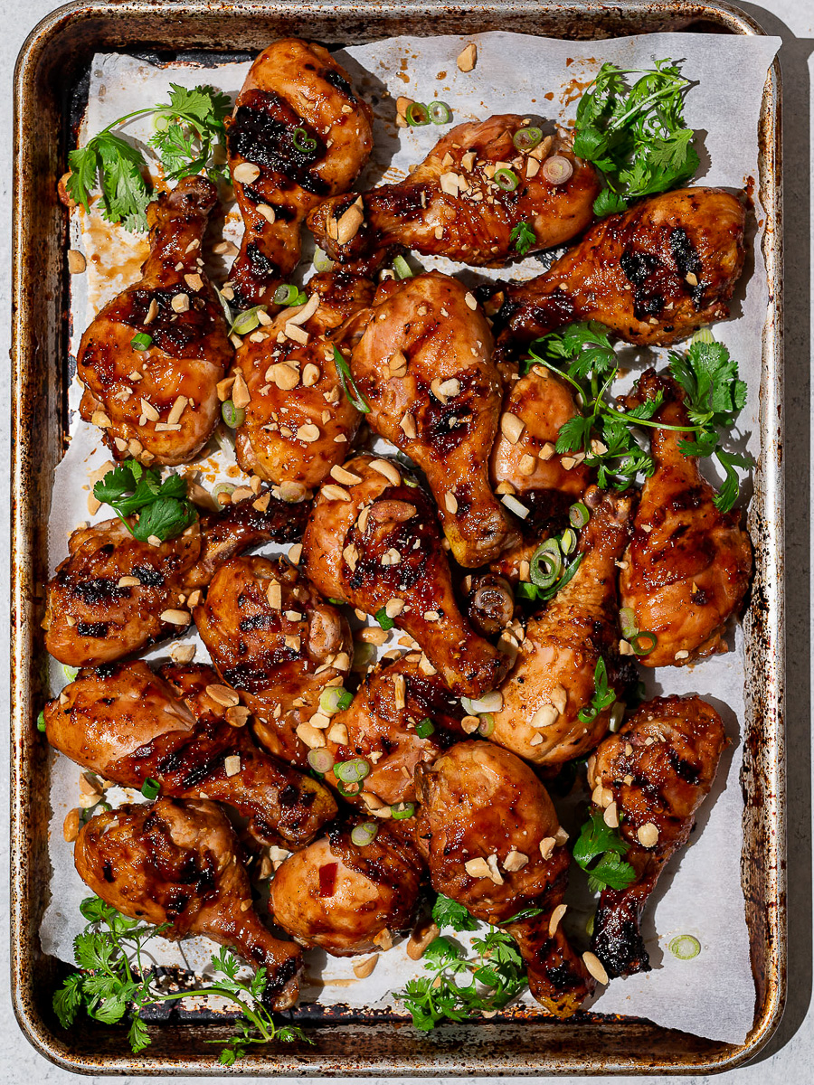 Grilled sticky sweet drumsticks on baking sheet garnished with chopped peanuts and fresh cilantro.