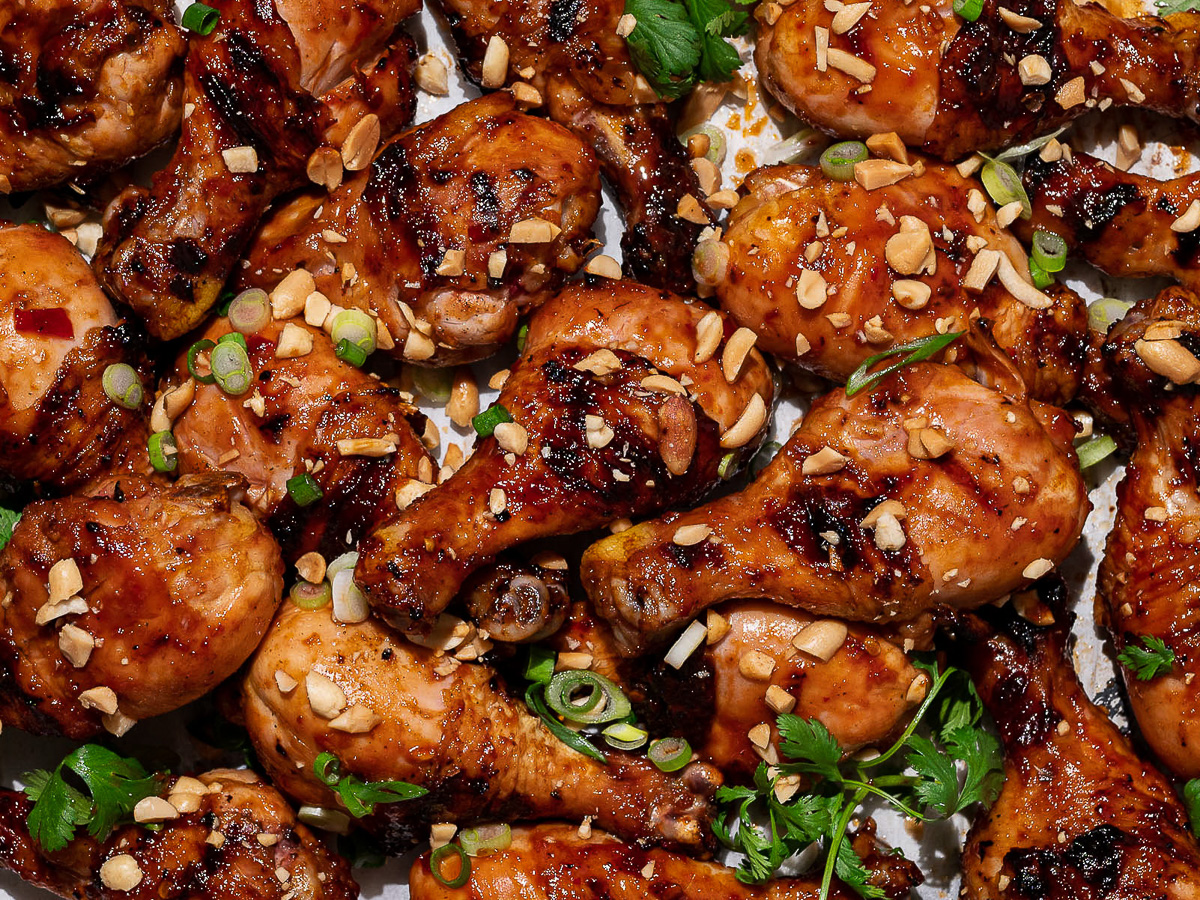 Close-up of grilled sticky sweet drumsticks garnished with chopped peanuts and cilantro.