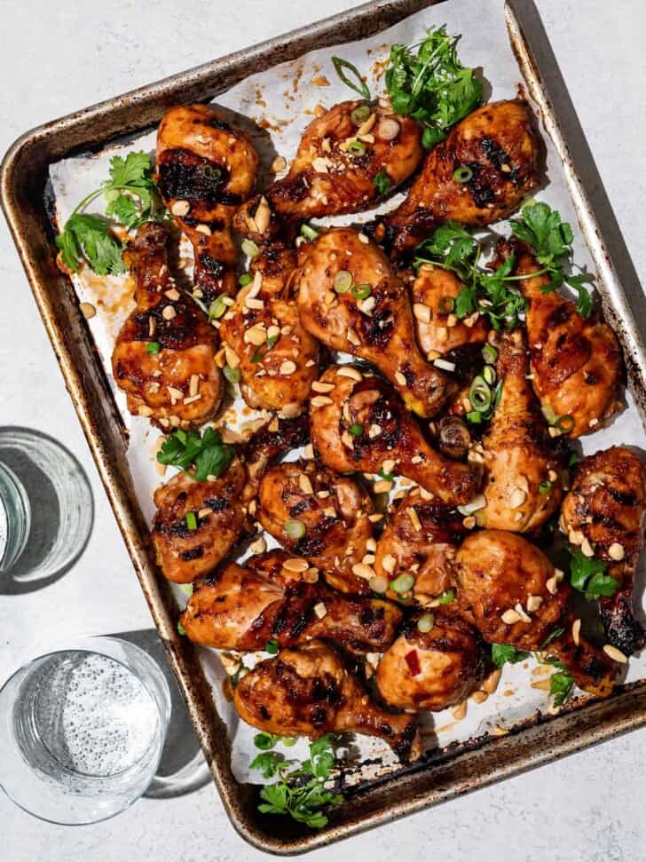 Sweet and sticky grilled drumsticks on sheet pan garnished with crushed peanuts, cilantro and scallions