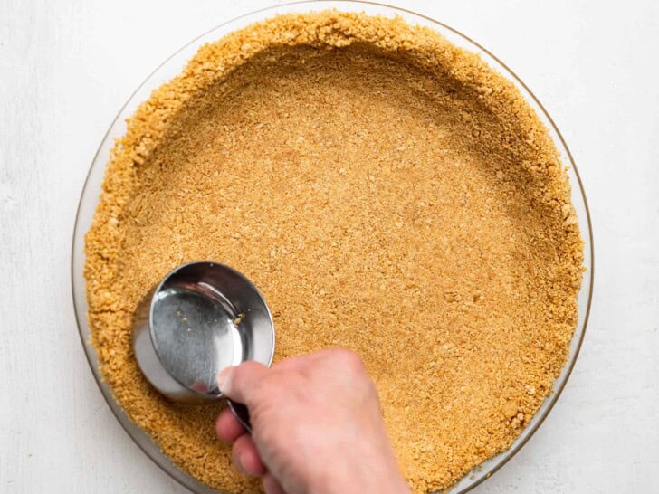 pressing crumbs into pie plate with measuring cup