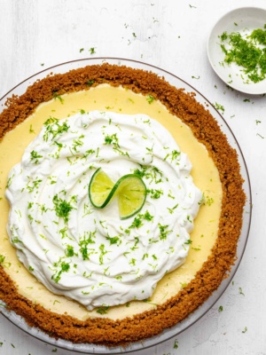 Baked key lime pie with whipped cream topping in pie plate lime zest on the side