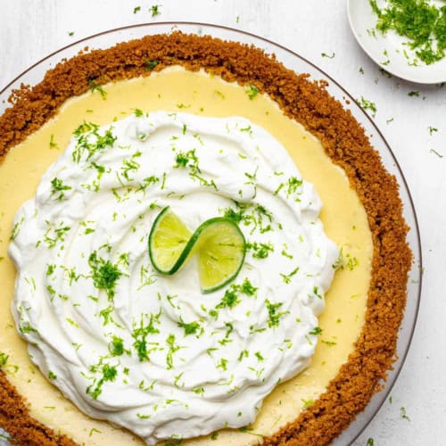 Baked key lime pie with whipped cream topping in pie plate lime zest on the side