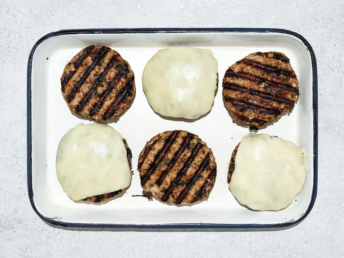 Six grilled poblano turkey patties on sheet pan, three of the patties topped with cheese. 