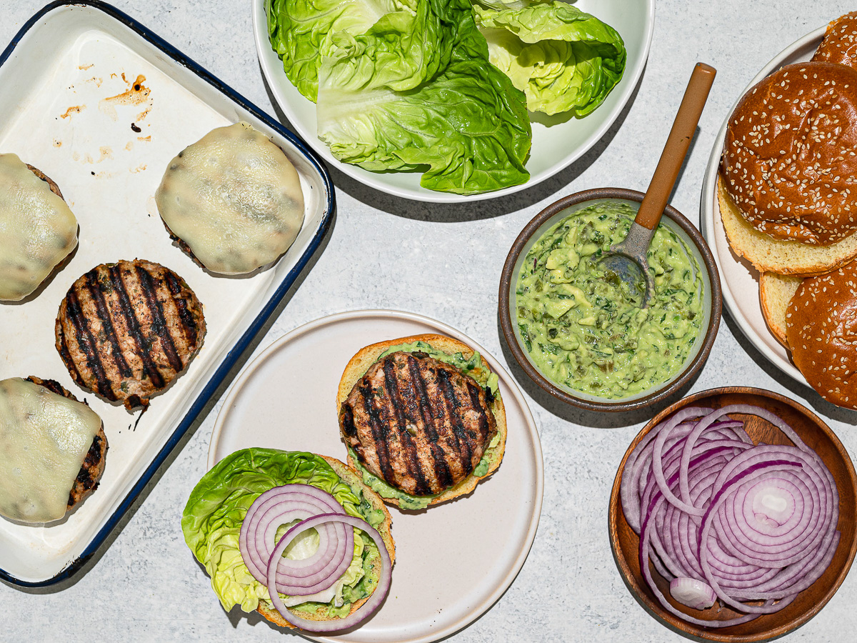 Topping burgers with lettuce, avocado sauce,  and sliced red onions. 