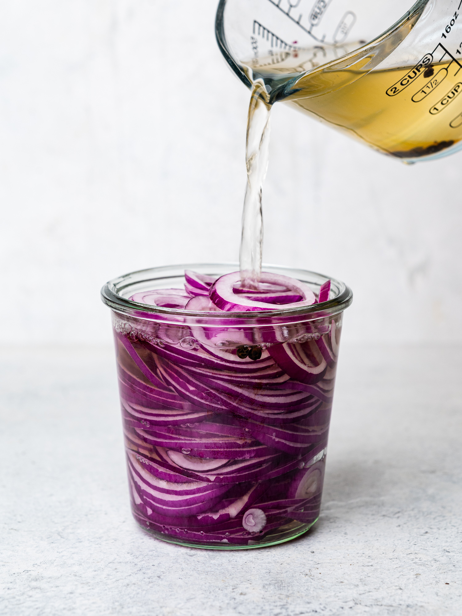 pouring brine over sliced onions in jar