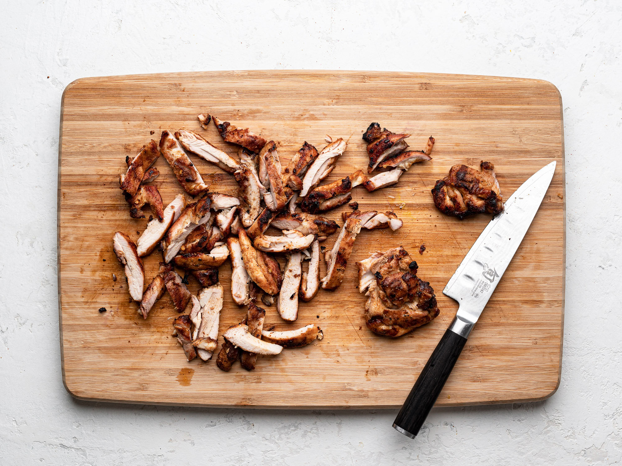 grilled chicken thighs on cutting board cut into strips