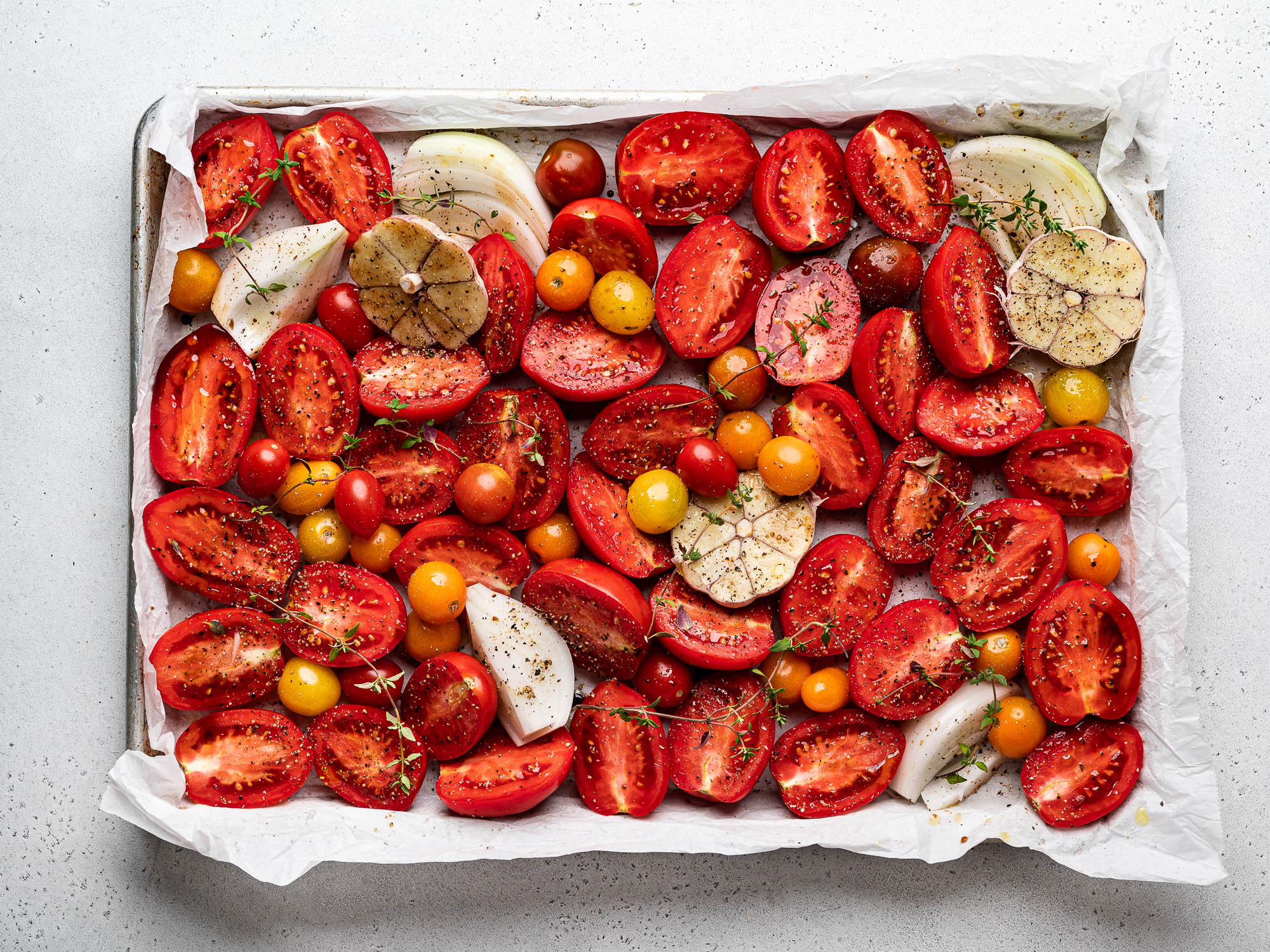 raw sliced tomatoes, onions, and garlic on sheet pan