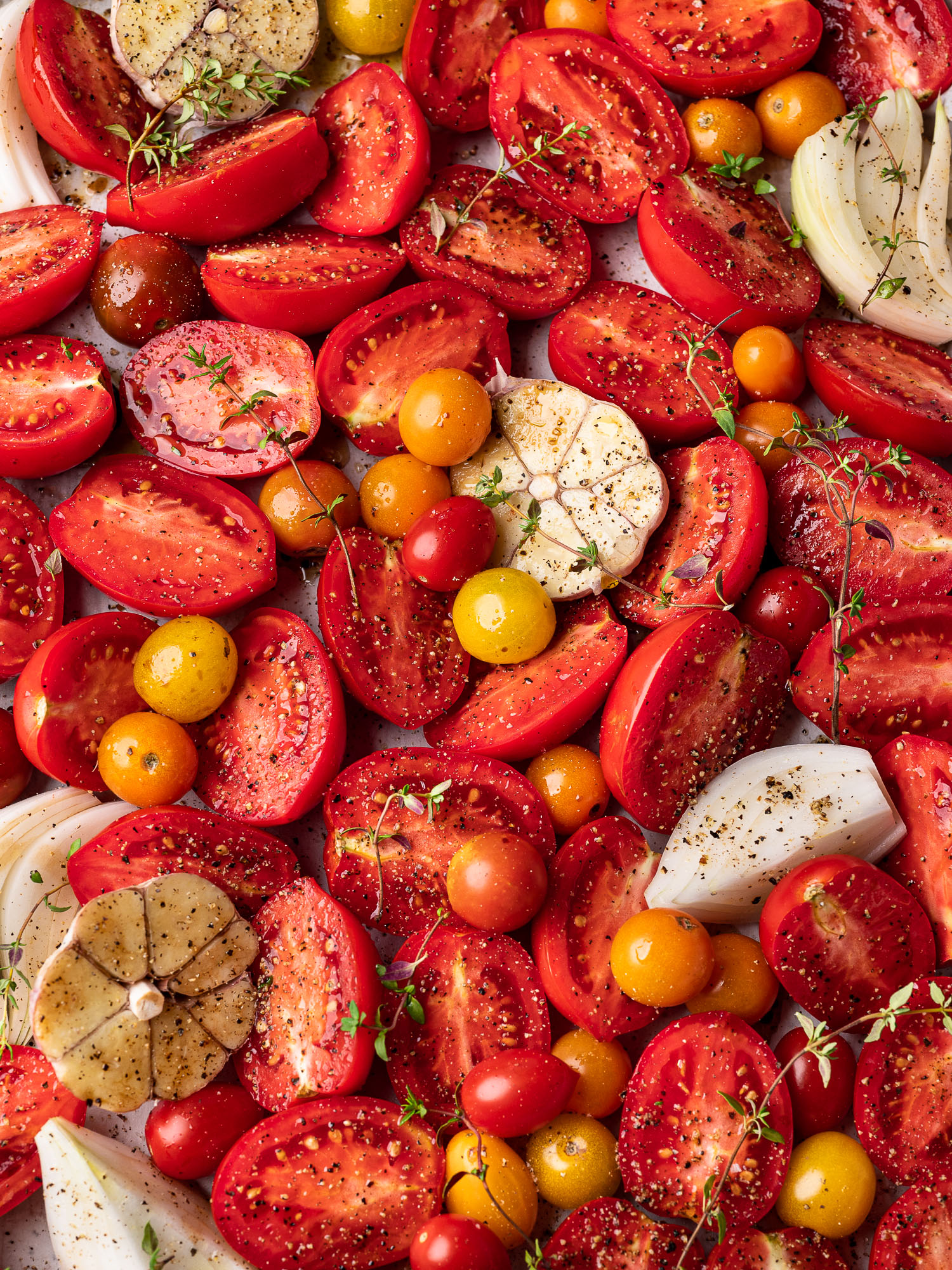 close-up of raw sliced tomatoes, onions, and garlic on sheet pan