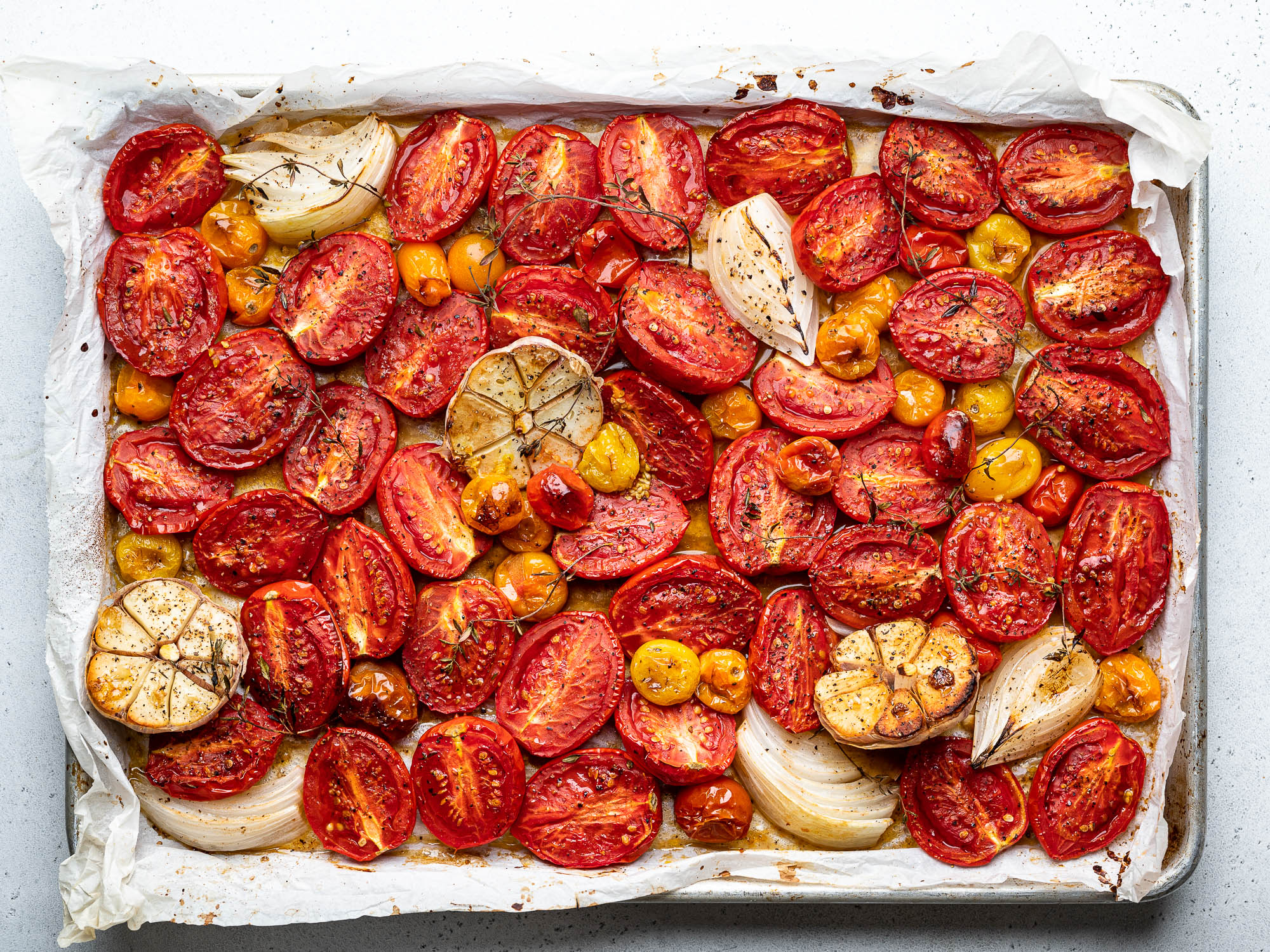 raw sliced tomatoes, onions, and garlic on sheet pan