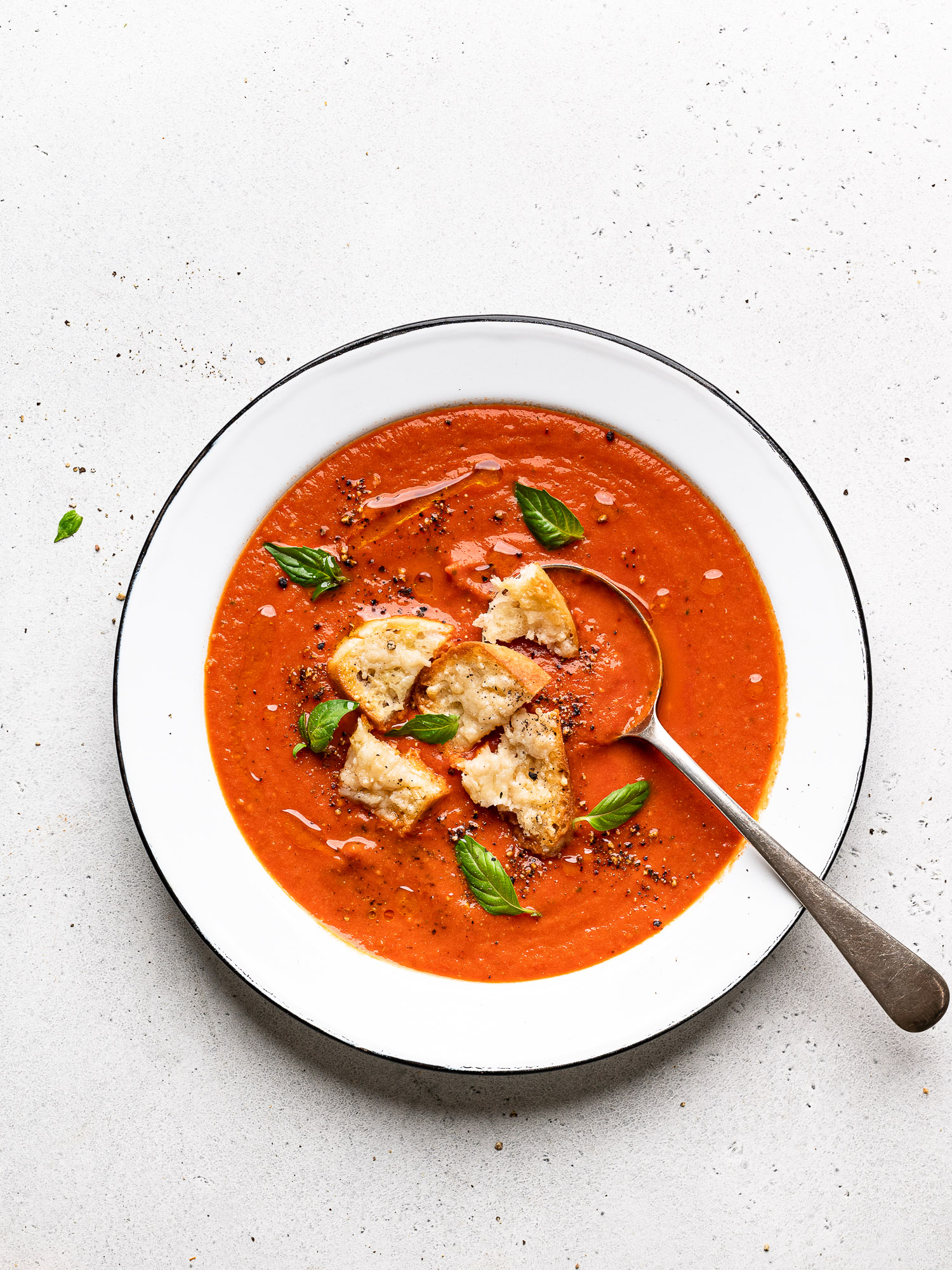 soup served in a shallow bowl and topped with parmesan toasts and fresh basil