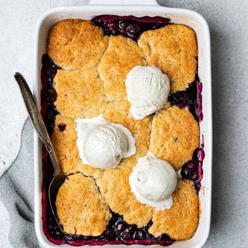 Blueberry cobbler in baking dish topped with 3 ice cream scoops