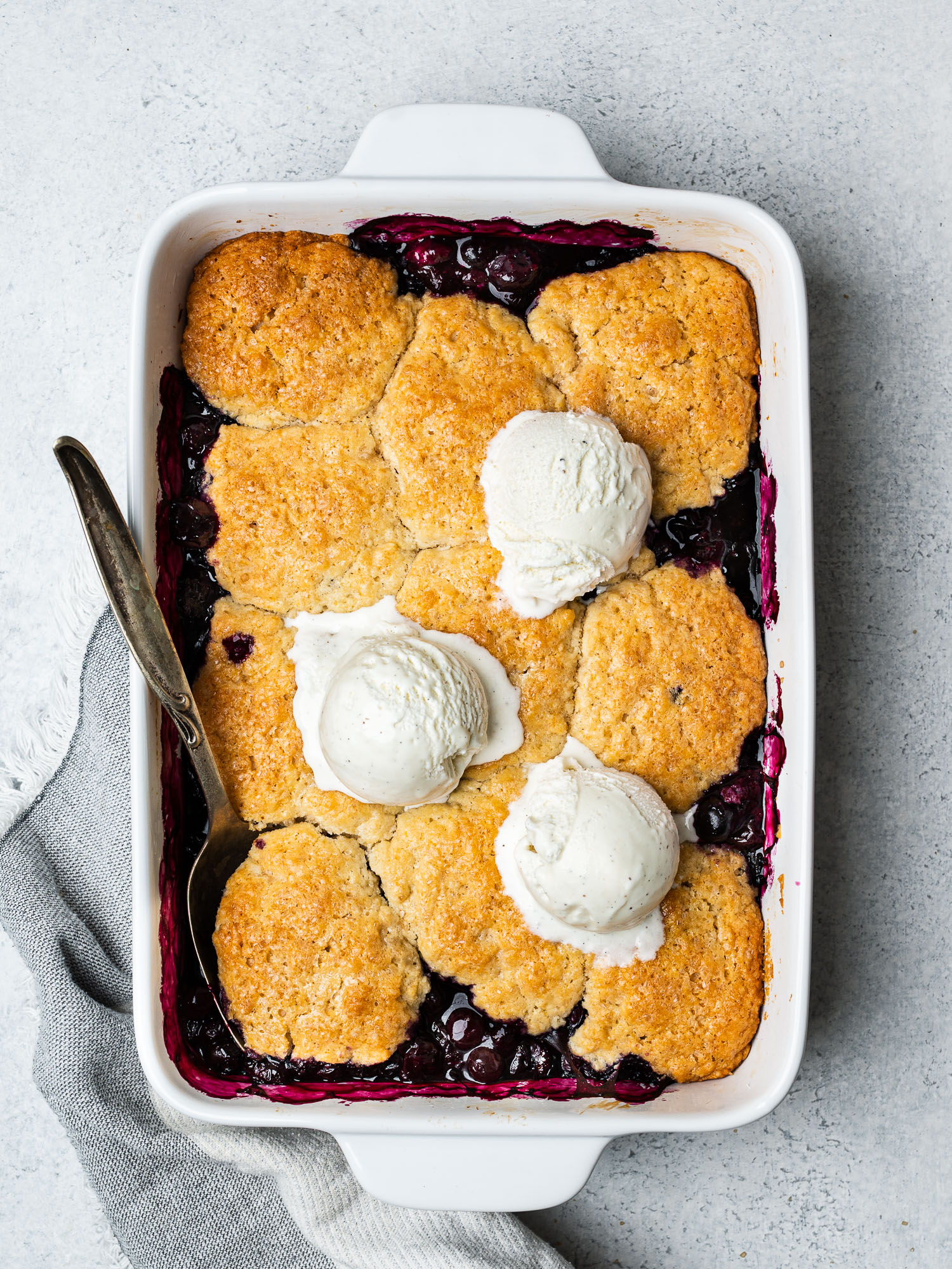 Blueberry cobbler in baking dish topped with 3 ice cream scoops