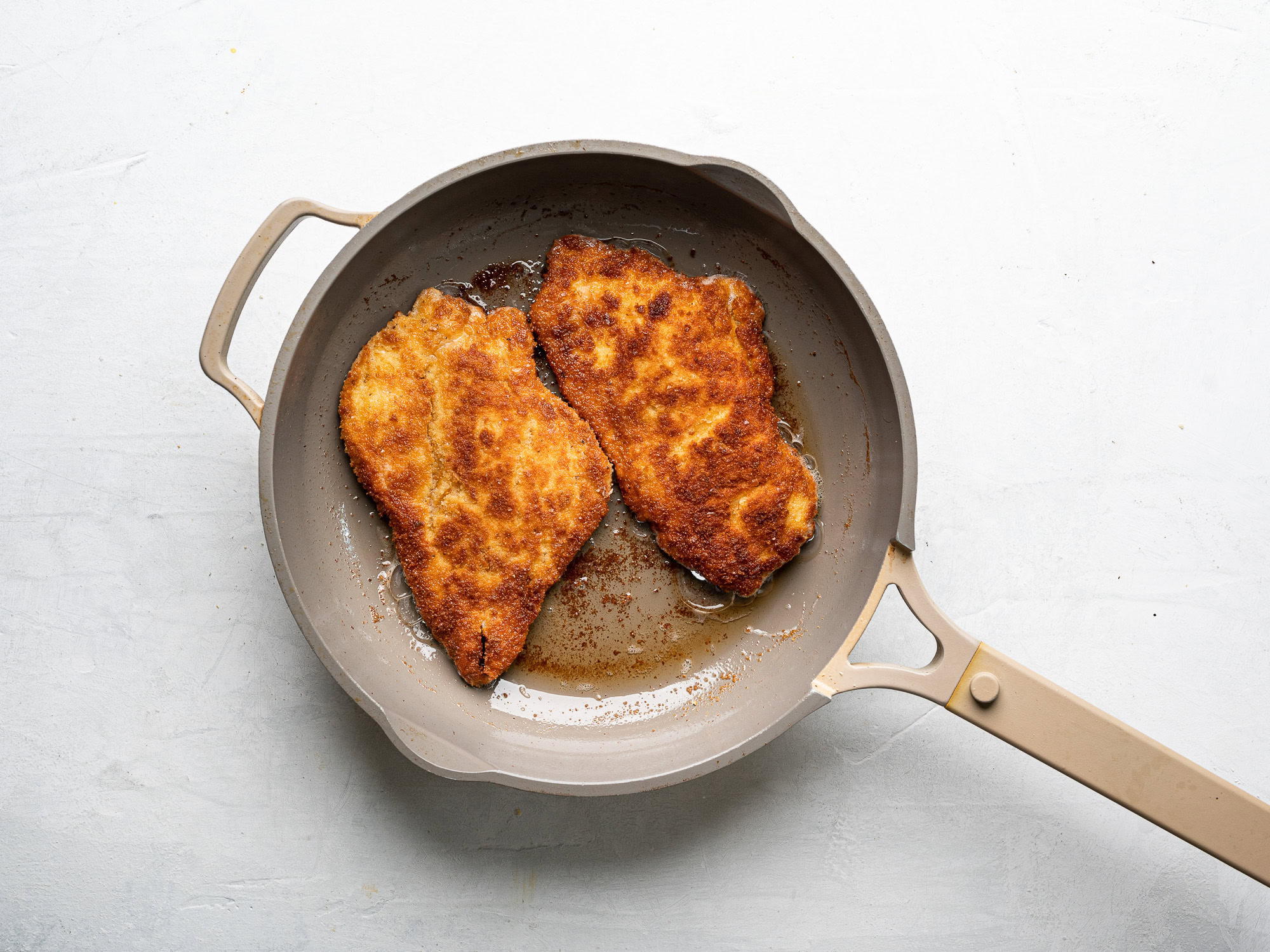 two cutlets frying in skillet