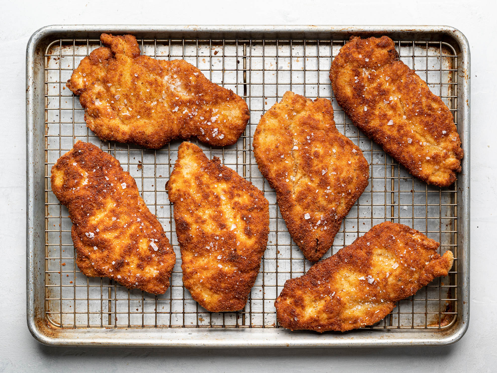 Breaded chicken milanese cutlets on baking rack with flaky salt