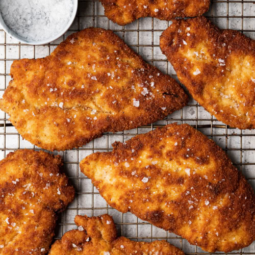 Breaded chicken milanese cutlets on baking rack with flaky salt