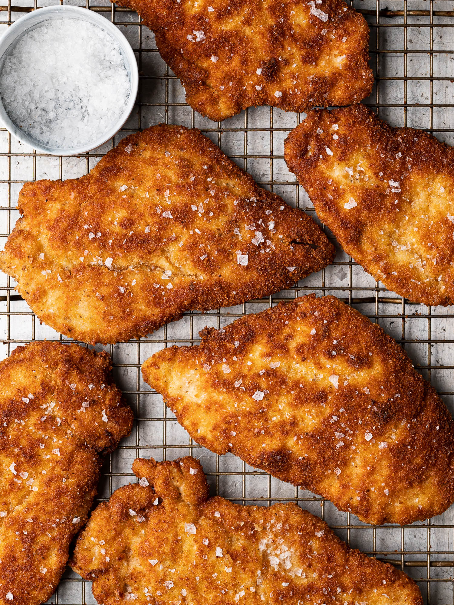 Breaded chicken milanese cutlets on baking rack with flaky salt