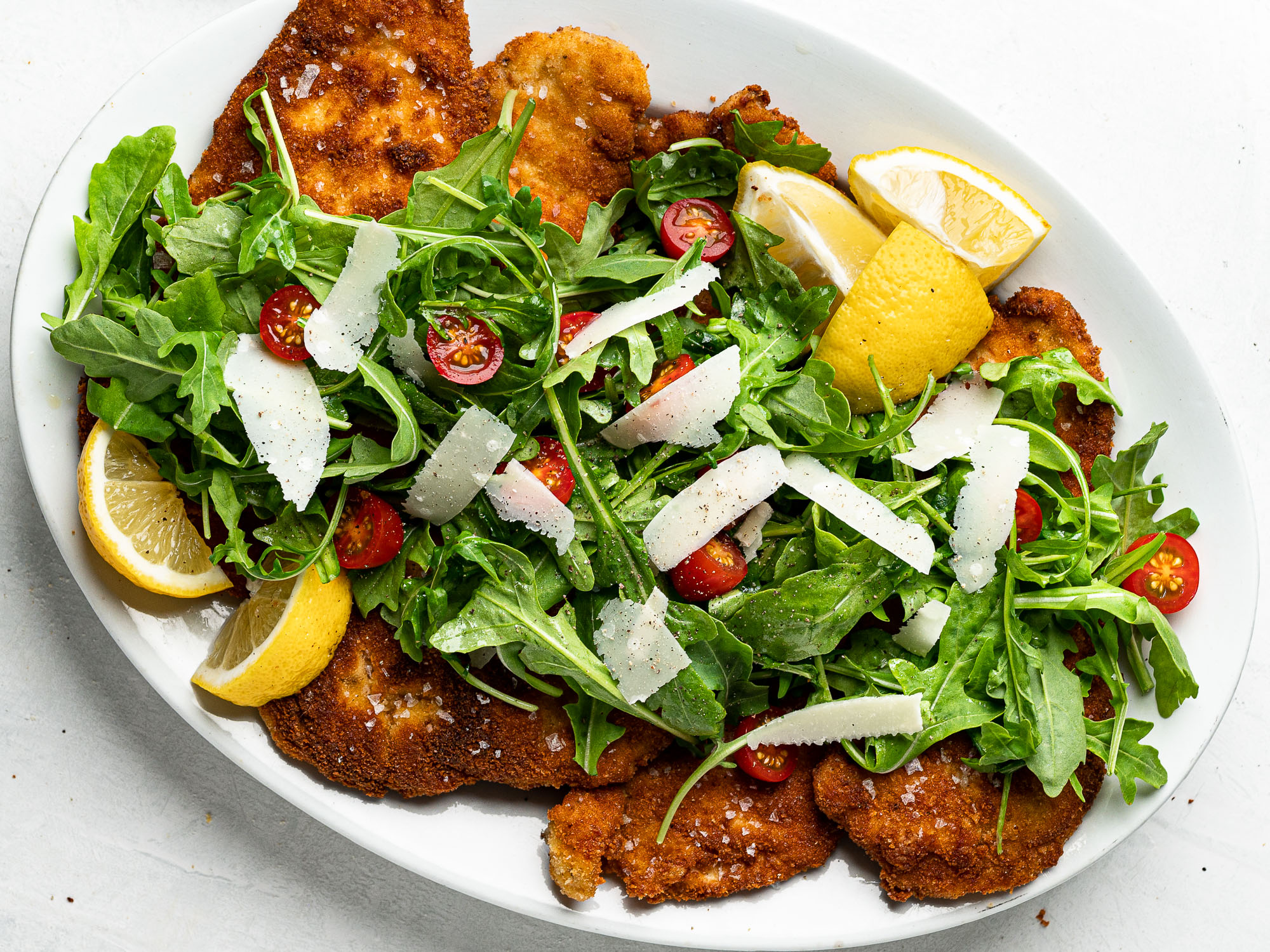 Chicken milanese served on platter topped with arugula salad