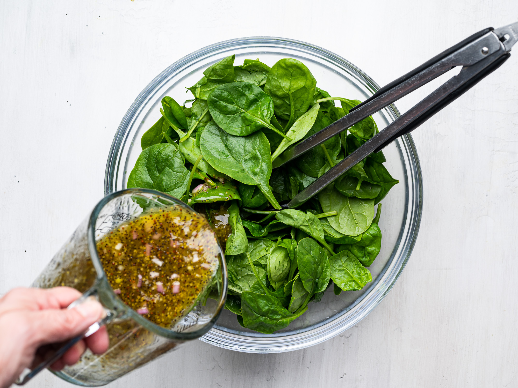 pouring dressing over spinach leaves in bowl