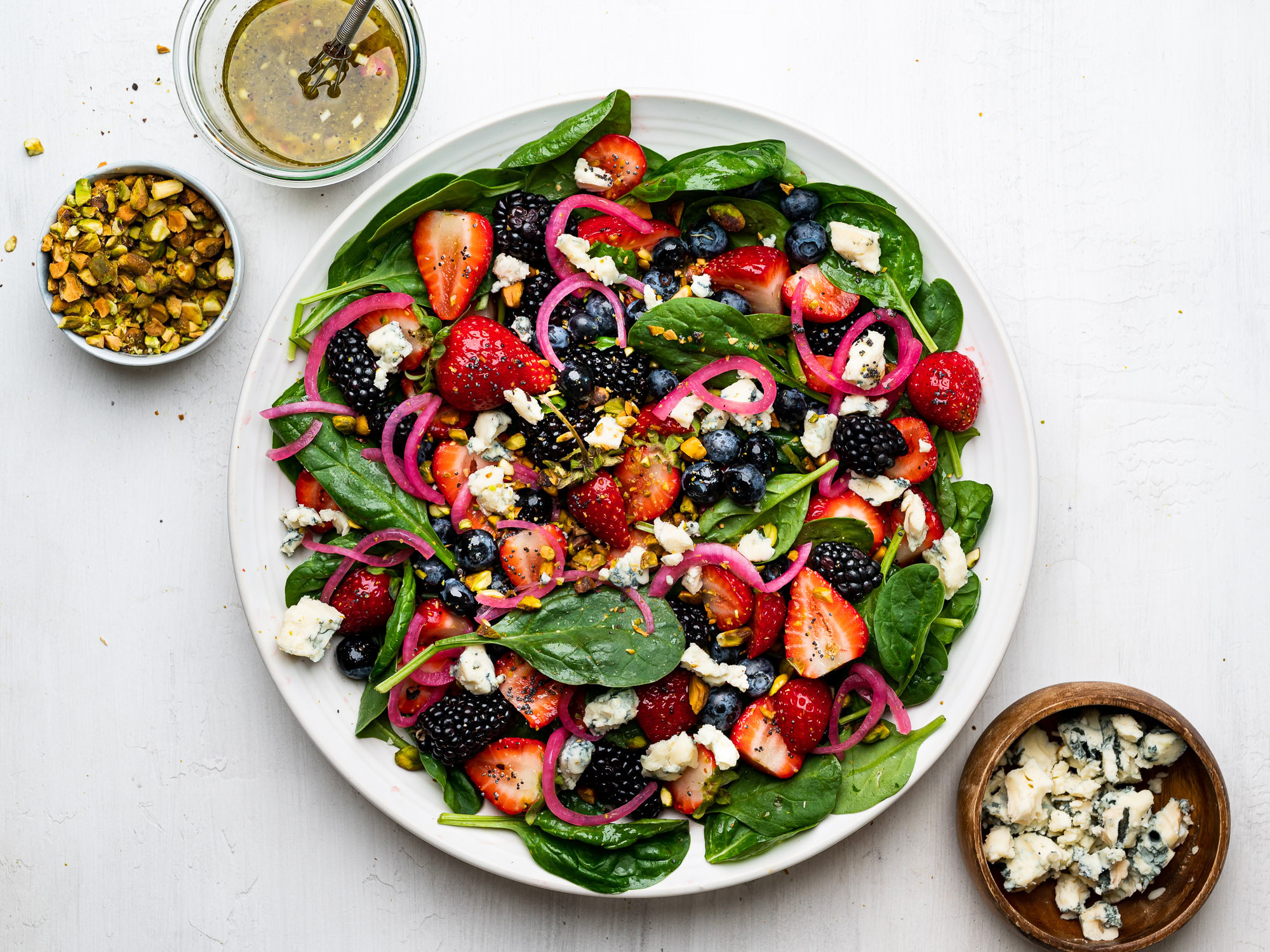 spinach berry salad served on platter and topped with pistachios, gorgonzola, and pickled red onions