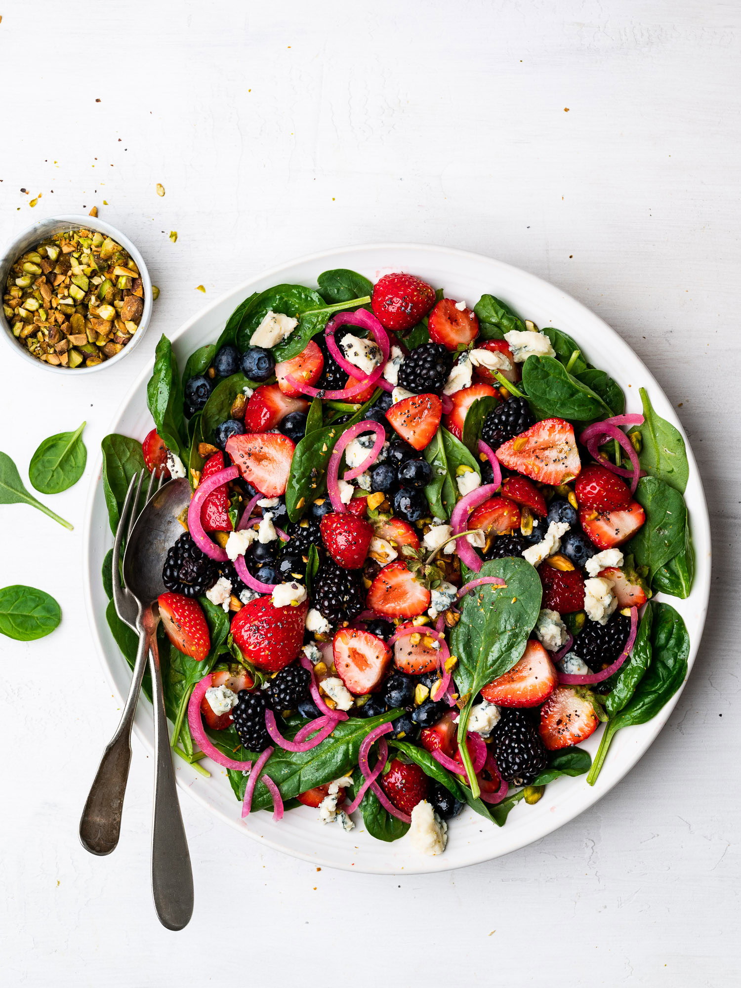 spinach berry salad served on platter and topped with pistachios, gorgonzola, and pickled red onions