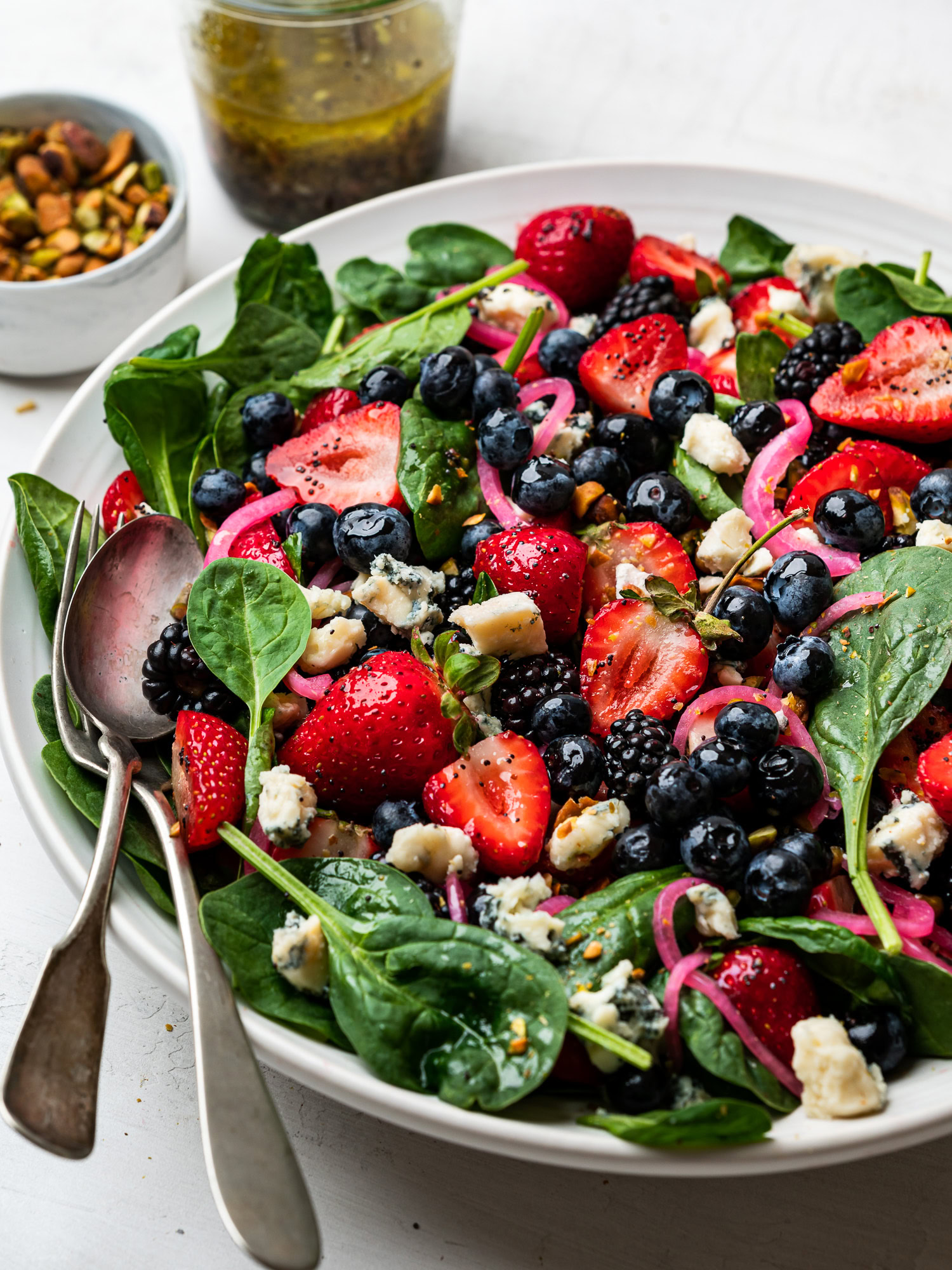 side view of spinach berry salad served on platter and topped with pistachios, gorgonzola, and pickled red onions