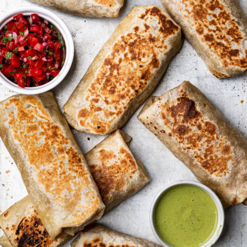 Bean and cheese burritos ready to eat on baking sheet with dipping sauces