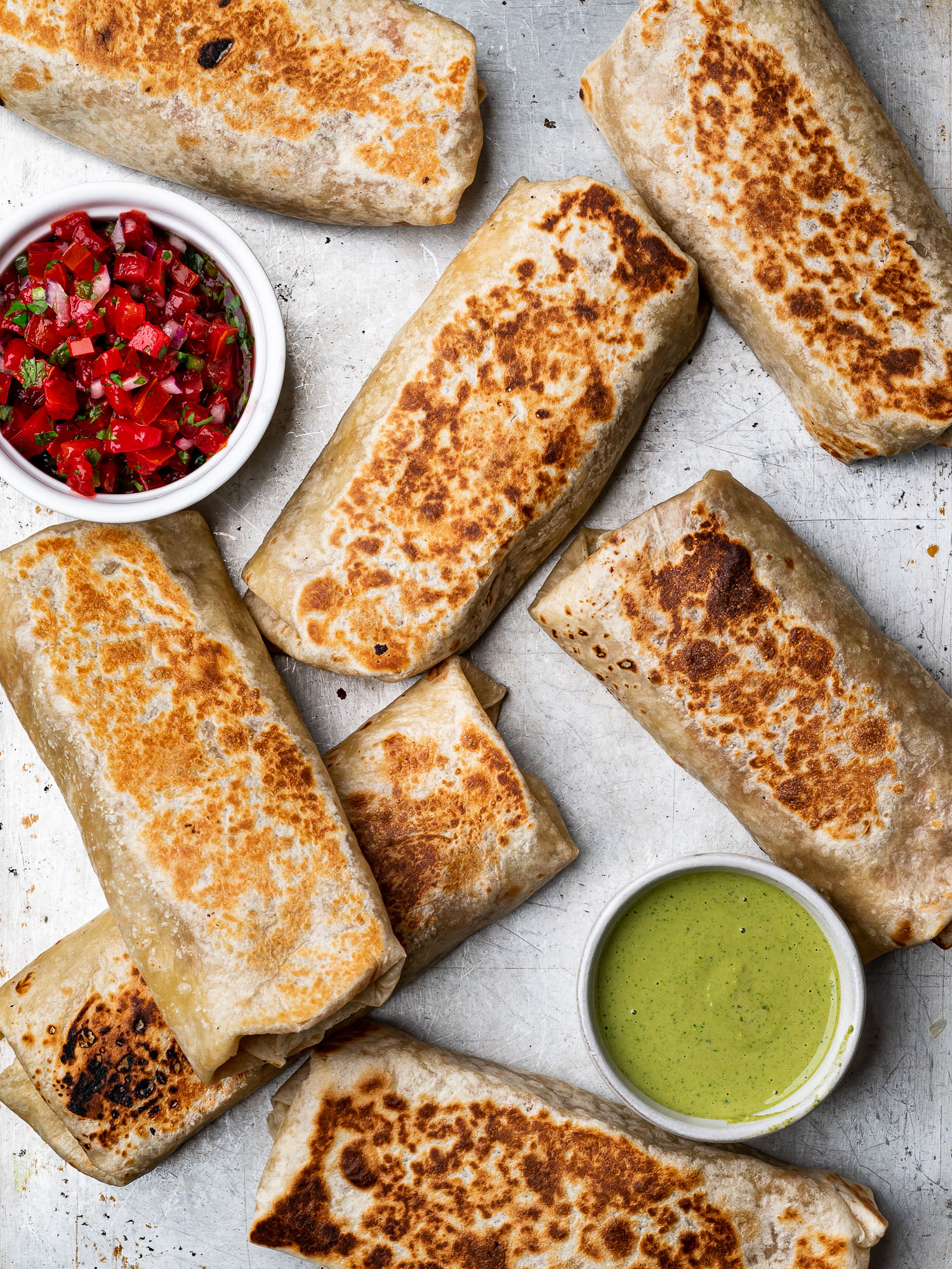 Bean and cheese burritos ready to eat on baking sheet with dipping sauces