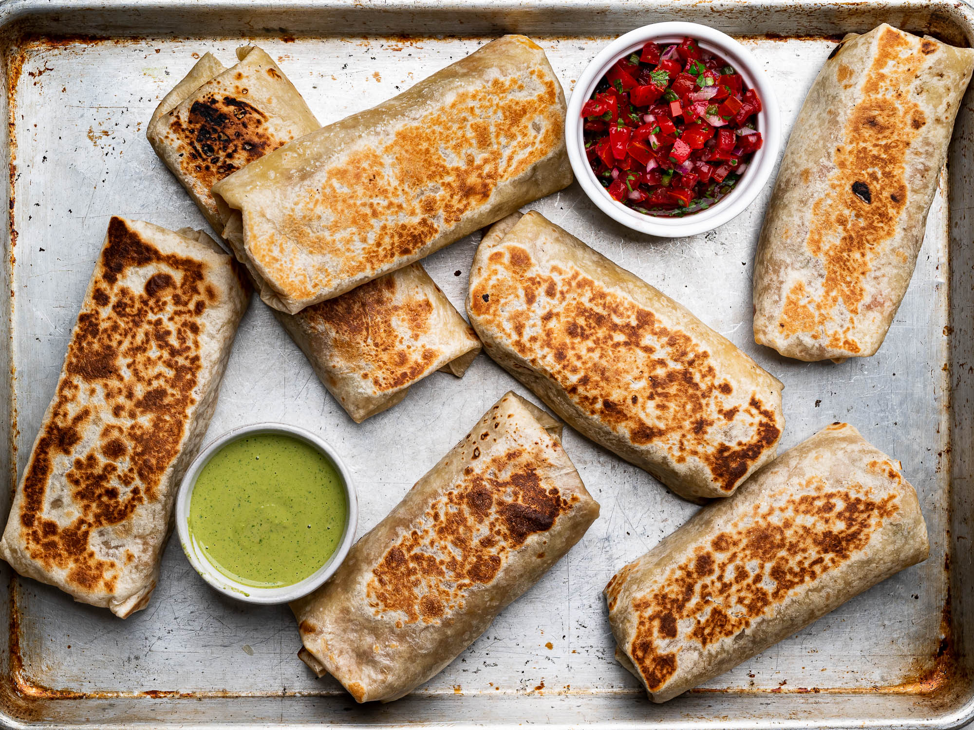 Bean and cheese burritos ready to eat on baking sheet with dipping sauces