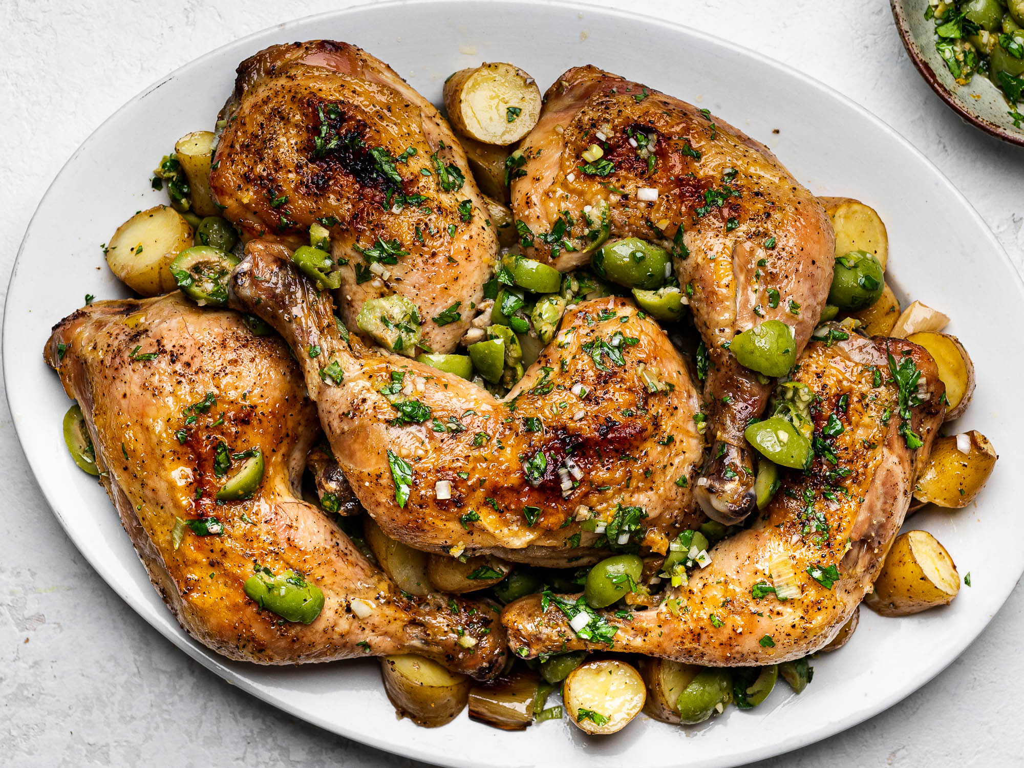 Chicken legs, leeks, and potatoes on a platter topped with green olive salsa