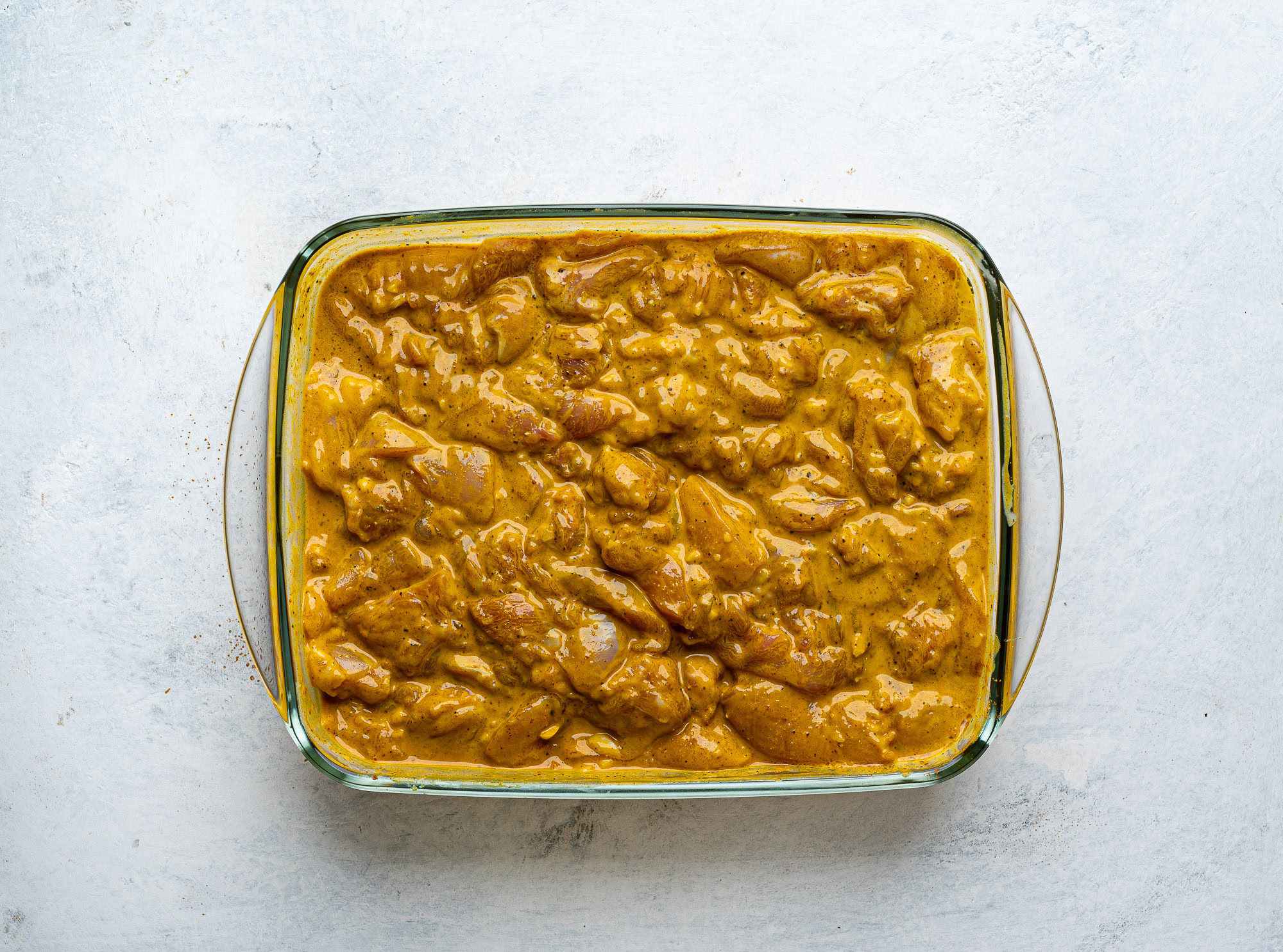 chicken thigh pieces marinating in glass container