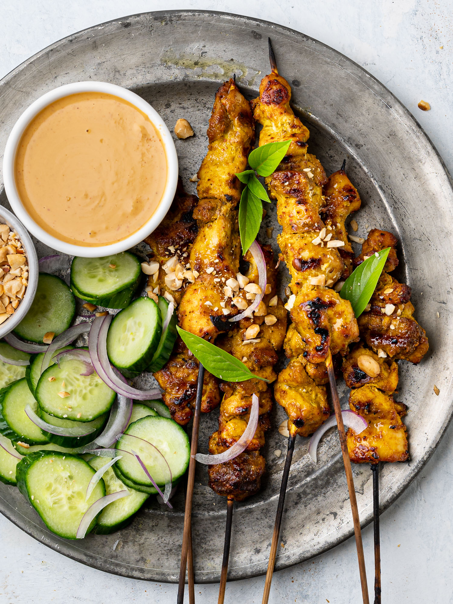 close up of chicken satay skewers on a plate with peanut dipping sauce and cucumber slices
