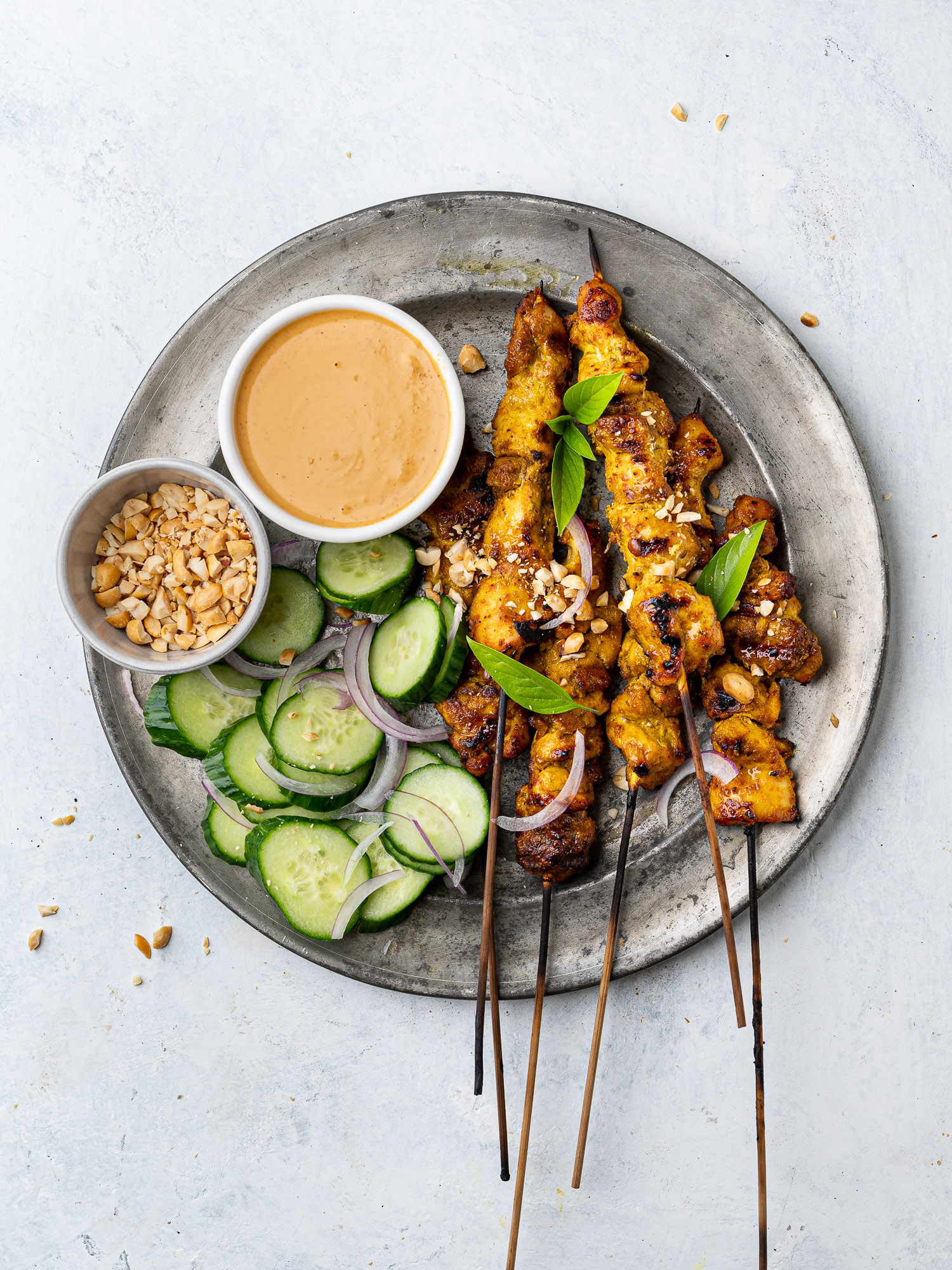 chicken satay skewers on a plate with peanut dipping sauce and cucumber slices
