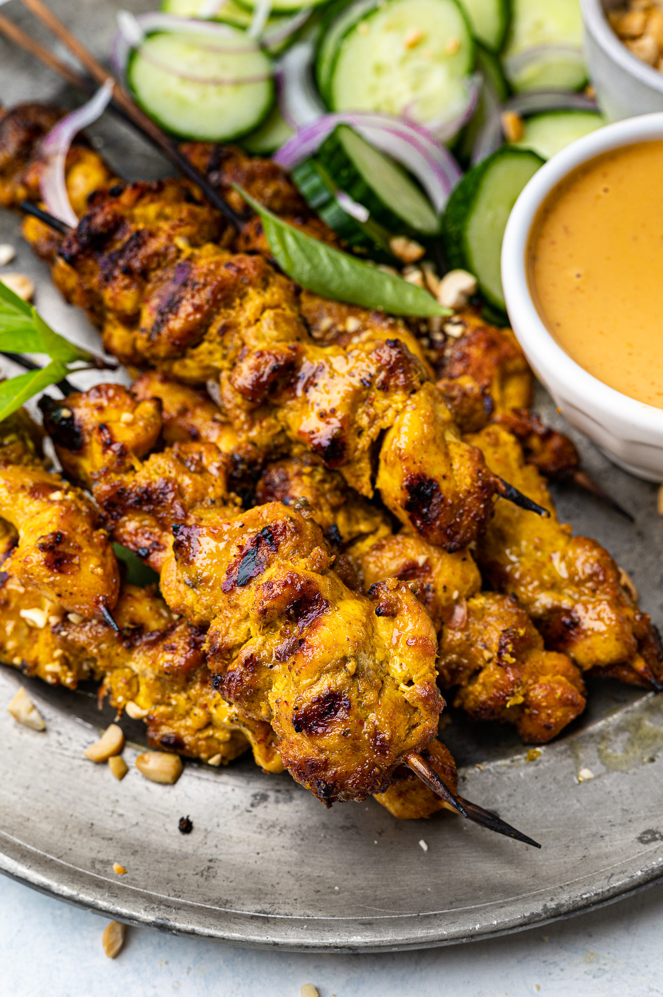 close up of chicken satay skewers on a plate with peanut dipping sauce and cucumber slices