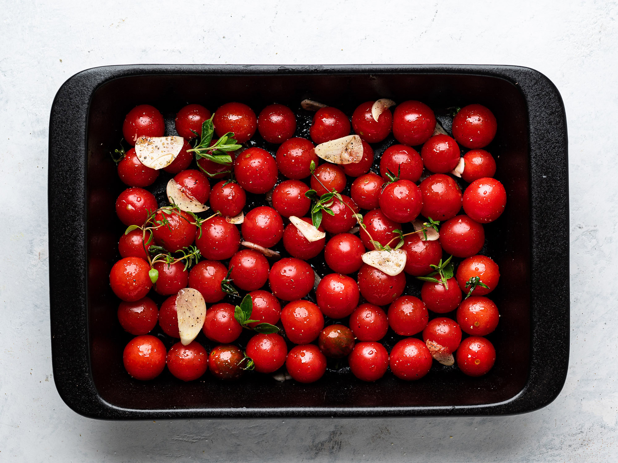 raw cherry tomatoes in baking dish with garlic and herbs