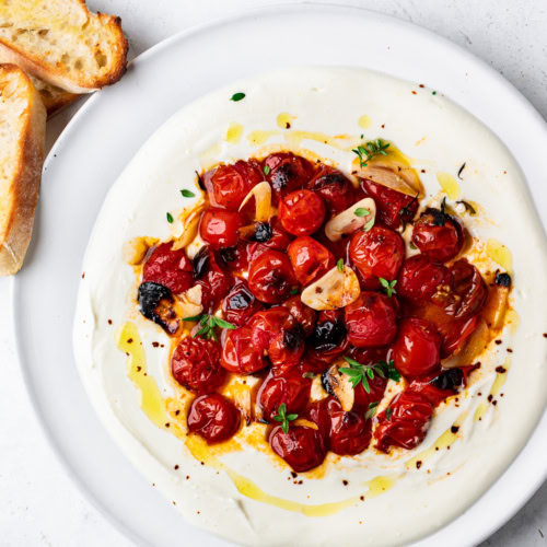 whipped feta with roasted cherry tomatoes on platter with toasted baguette