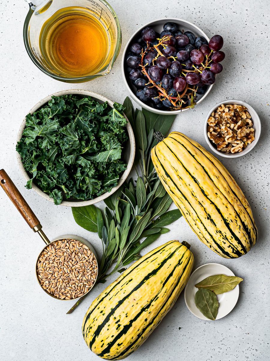 Ingredients needed for recipe, including whole delicata squash, kale, grapes, and farro.