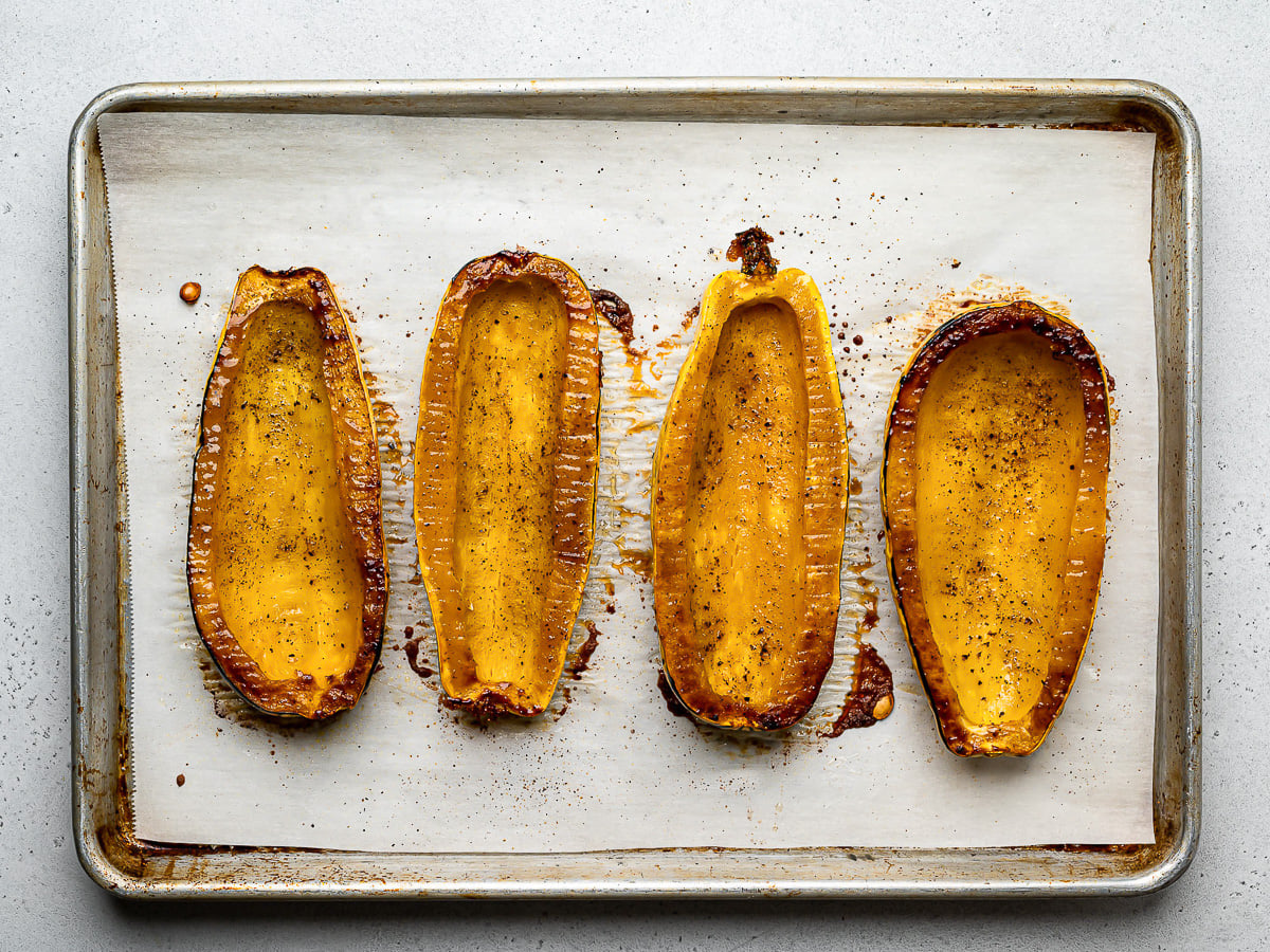 Four roasted delicata squash halves on baking sheet.