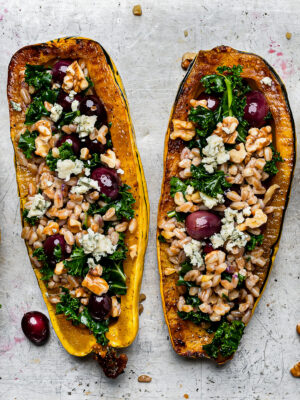 Cloesup of two roasted Delicata squash halves stuffed with farro mixture.