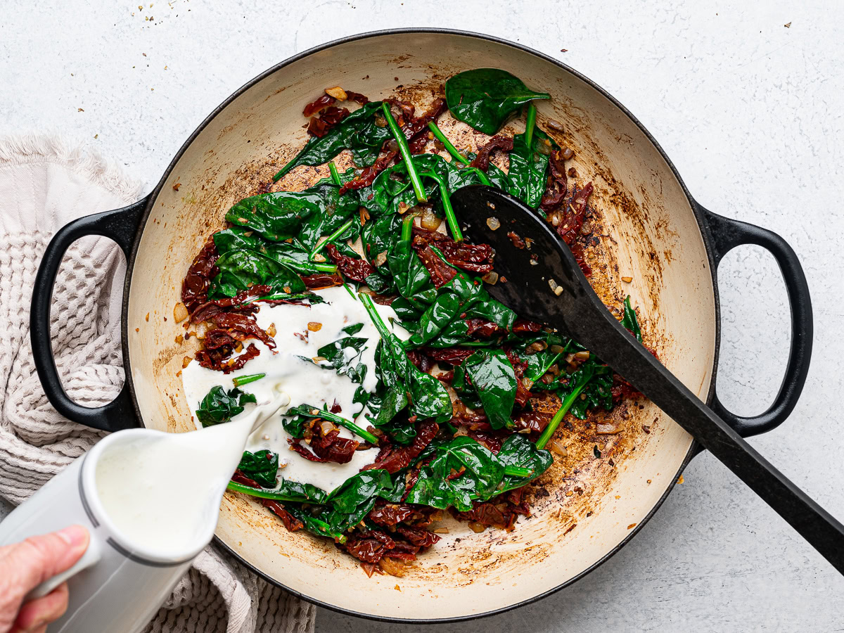 adding heavy cream to spinach mixture in skillet