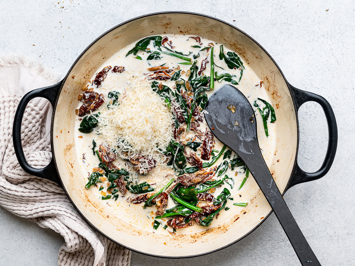 adding parmesan to cream sauce in skillet