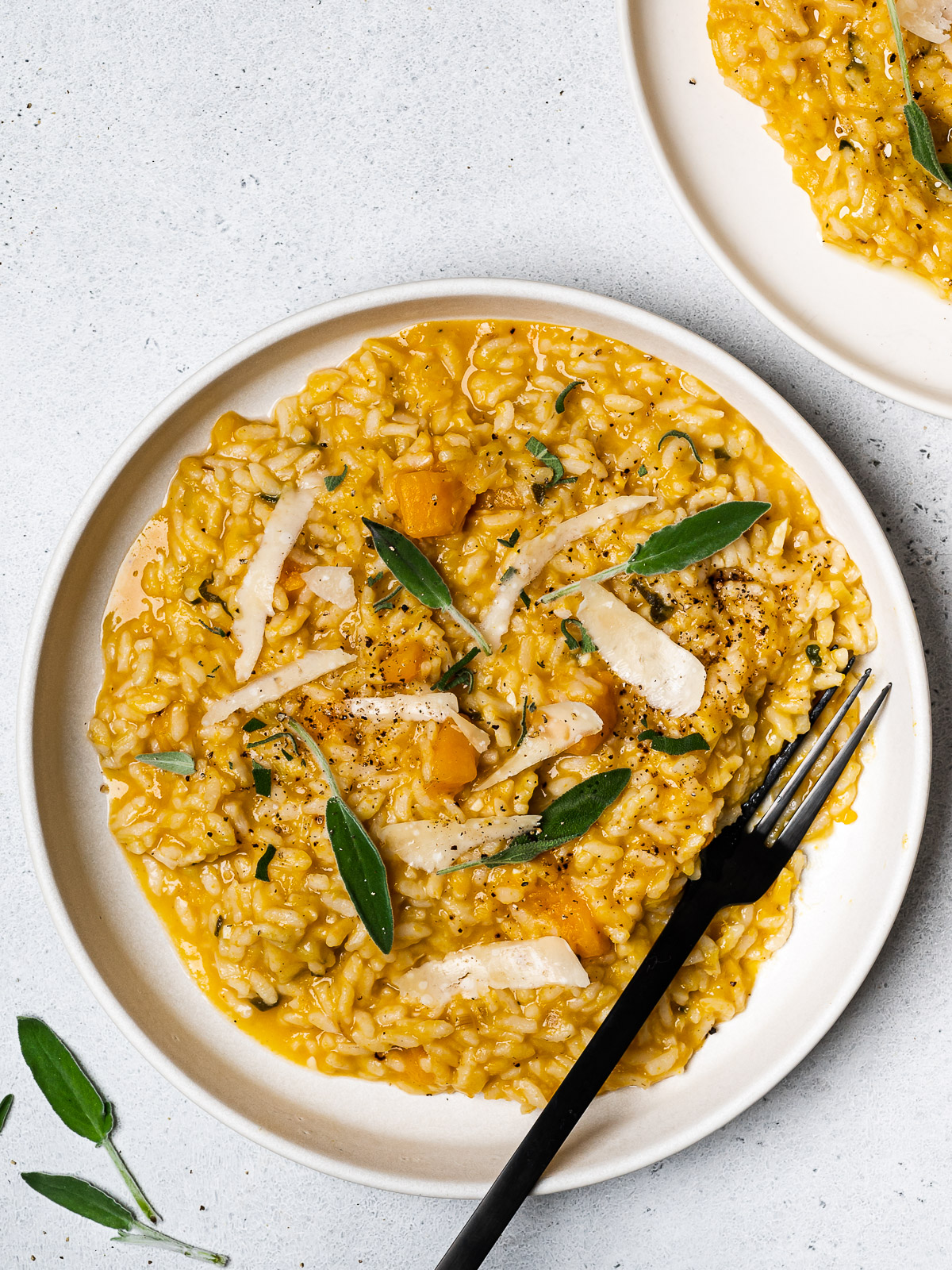 butternut squash risotto served on two plates topped with fresh sage leaves
