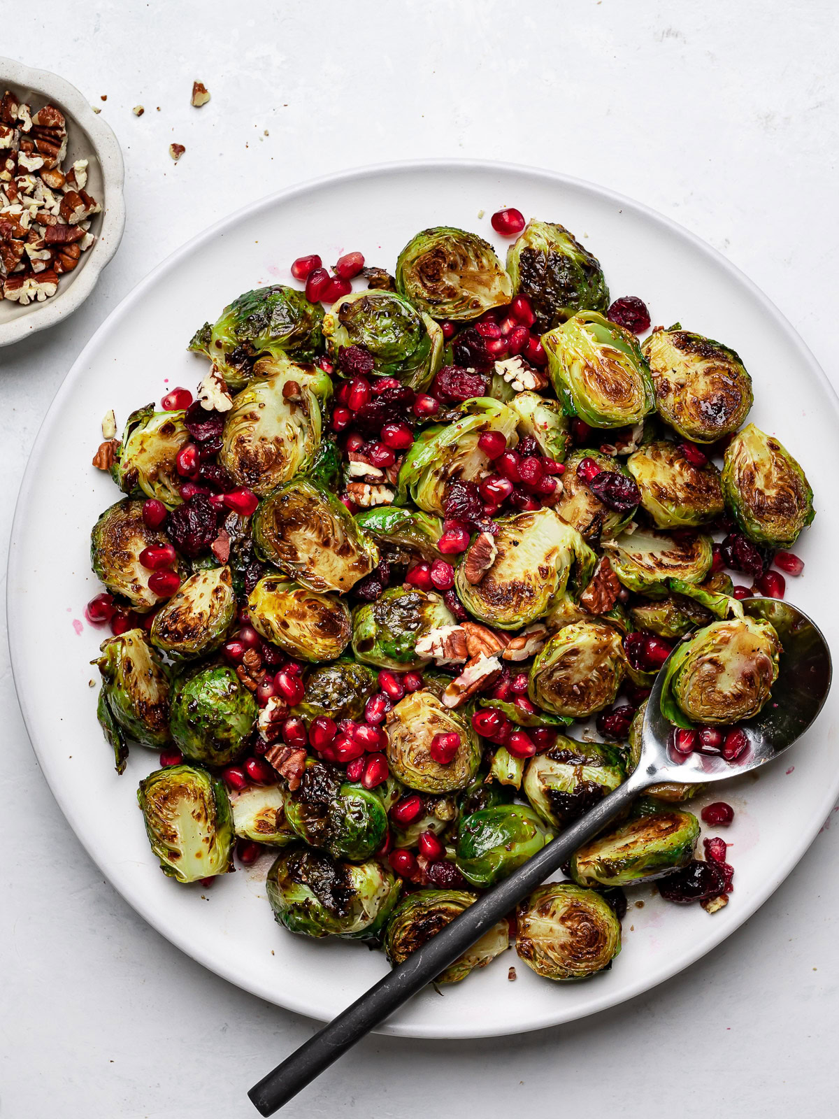 Roasted Brussels sprouts tossed with pecans, pomegranate seeds and a balsamic glaze on a platter