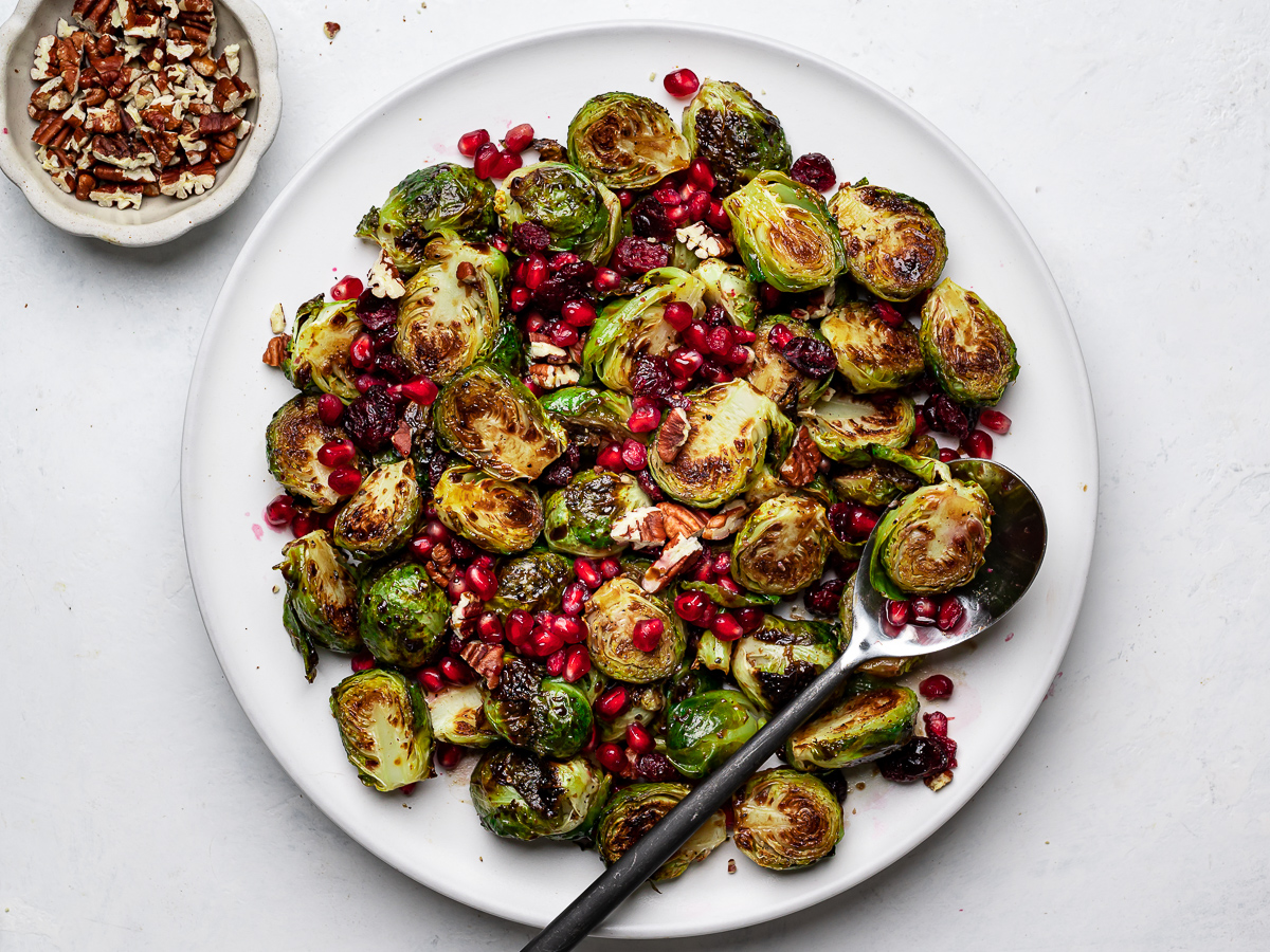 Roasted Brussels sprouts tossed with pecans, pomegranate seeds and a balsamic glaze on a platter