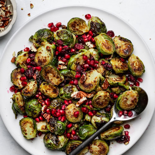Roasted Brussels sprouts tossed with pecans, pomegranate seeds and a balsamic glaze on a platter