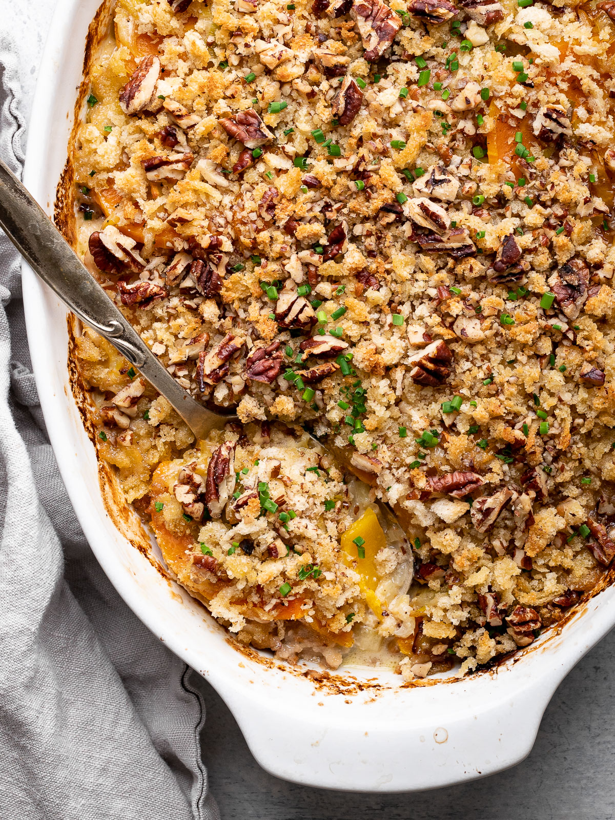 Close-up of spoon scooping out a piece of butternut squash gratin from baking dish