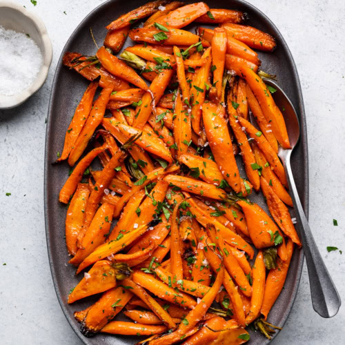 Honey Maple Roasted Carrots served on platter garnished with parsley and flaky salt