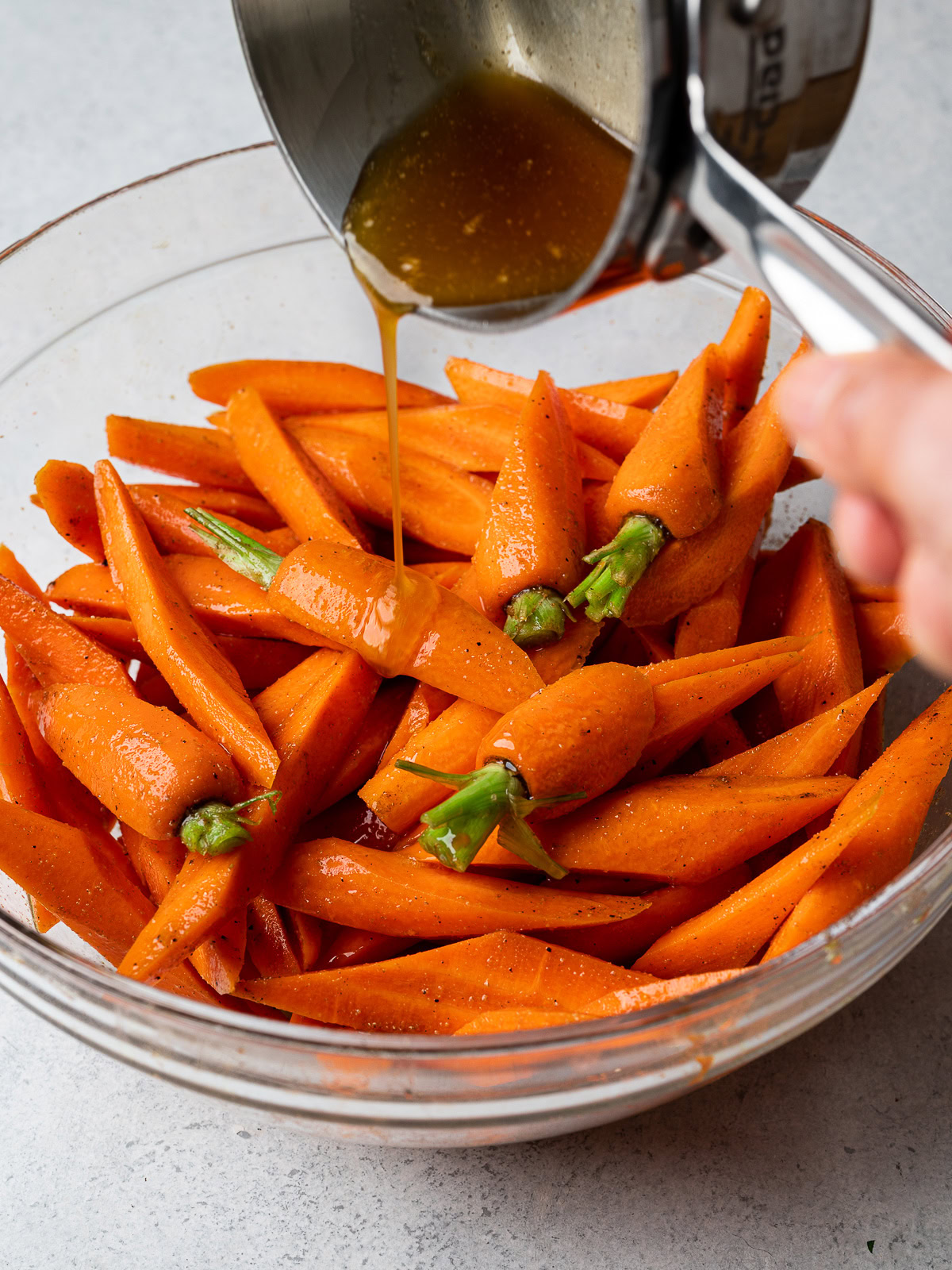 pouring glaze over sliced carrots in bowl